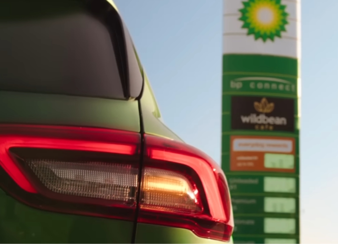 Close-up of a car’s rear light at a BP petrol station with fuel price sign in the background.