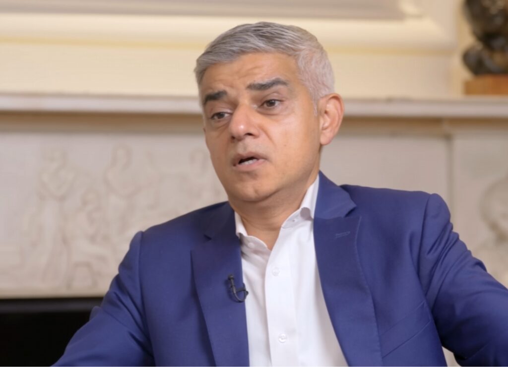 London Mayor Sadiq Khan speaking during an indoor interview, wearing a blue suit jacket and white shirt.