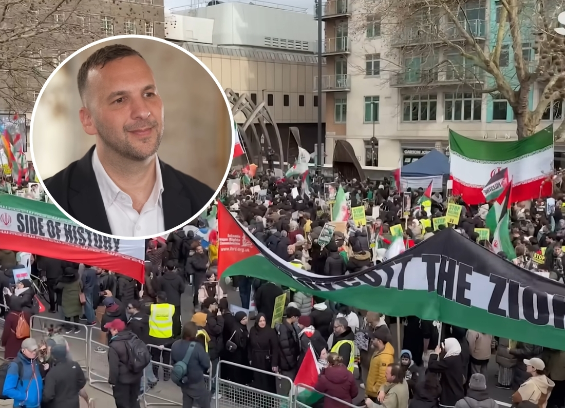 A large crowd of protesters in a city square holding Iranian and Palestinian flags, with a circular inset image of Green Party leader Zack Polanski in a dark blazer.