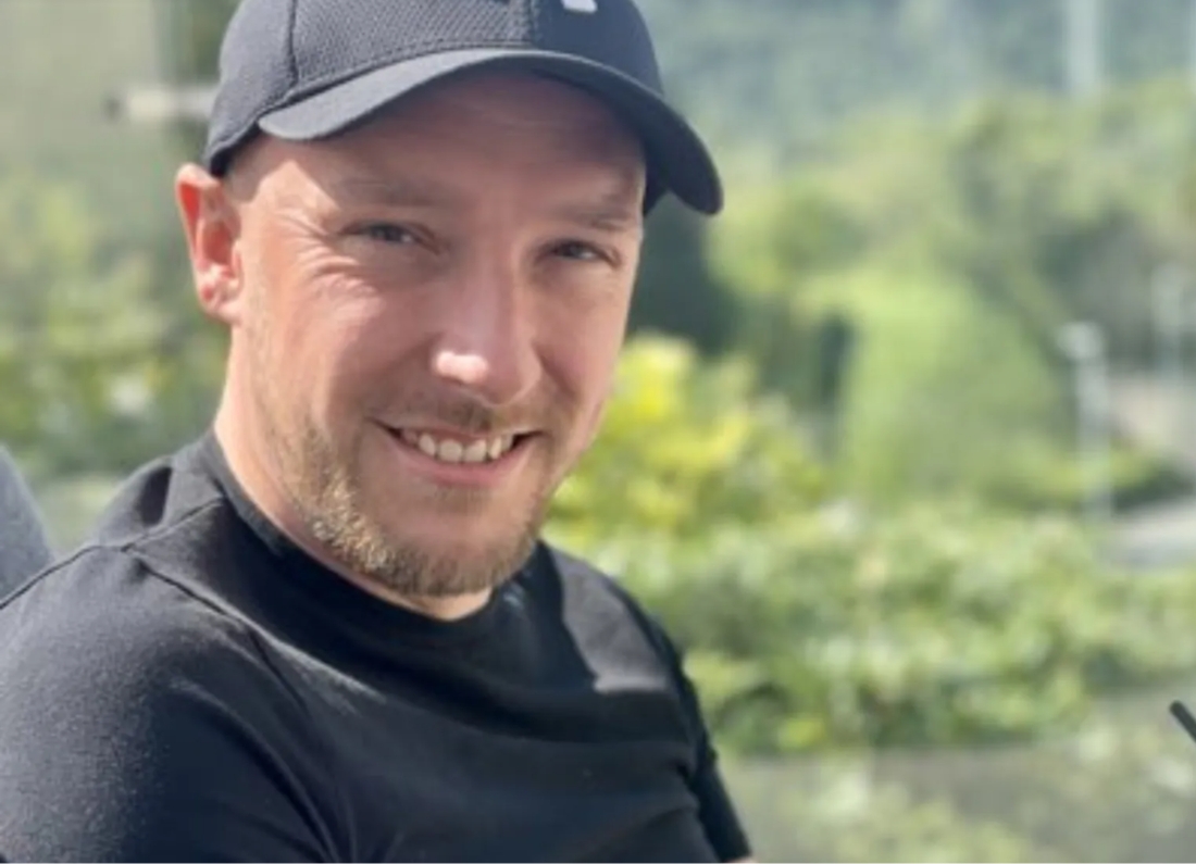 Newly elected Reform UK councillor Stephen Mousdell smiles while wearing a black cap and black shirt outdoors.
