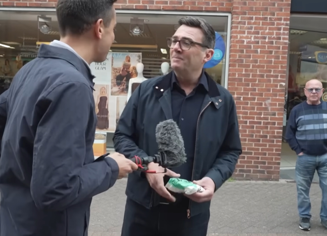 Greater Manchester Mayor Andy Burnham being interviewed by a reporter on a shopping street while discussing speculation about Labour leadership ambitions.