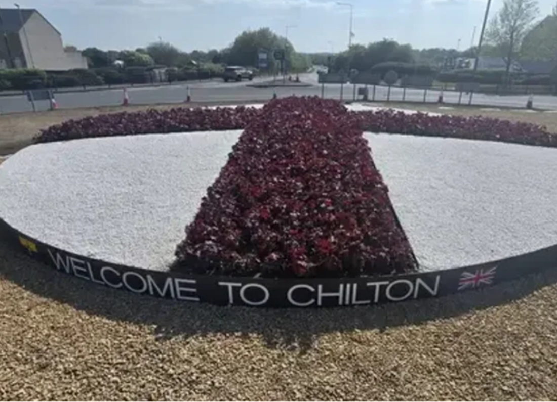 Roundabout display in Chilton featuring a floral St George’s cross with a “Welcome to Chilton” sign.