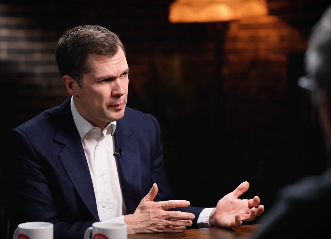 Robert Jenrick speaking during a studio interview while gesturing with his hands across a table.