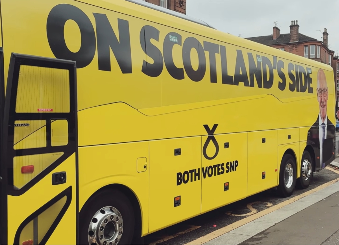 A bright yellow SNP campaign bus parked on a street in Scotland.