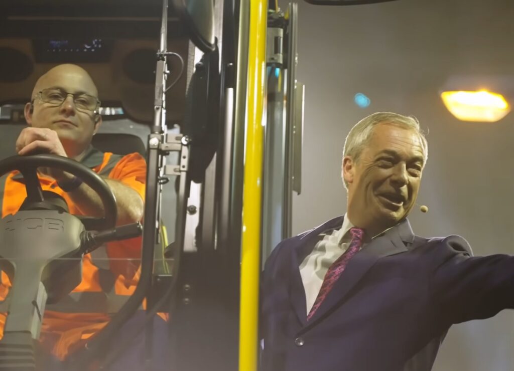 Nigel Farage stands beside a large vehicle while a worker in high-visibility orange clothing sits in the driver's seat. The scene appears to take place at an industrial or agricultural event under bright lights.