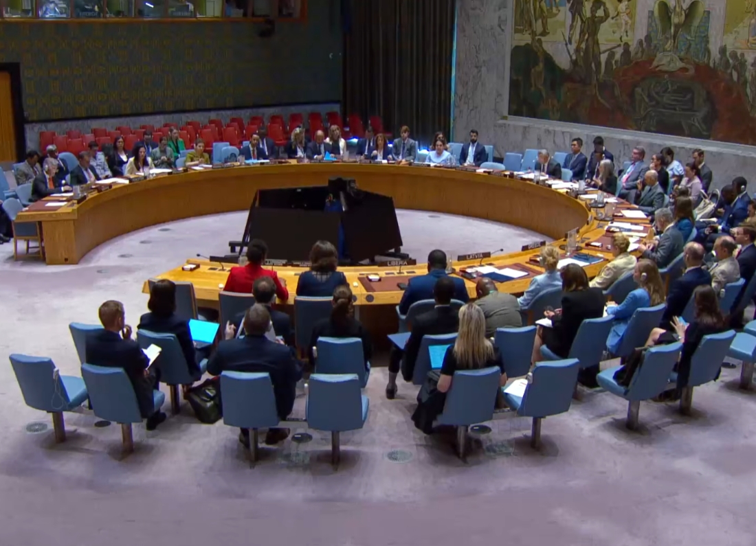 Wide shot of the United Nations Security Council chamber during a formal international meeting with diplomats seated around a circular table.