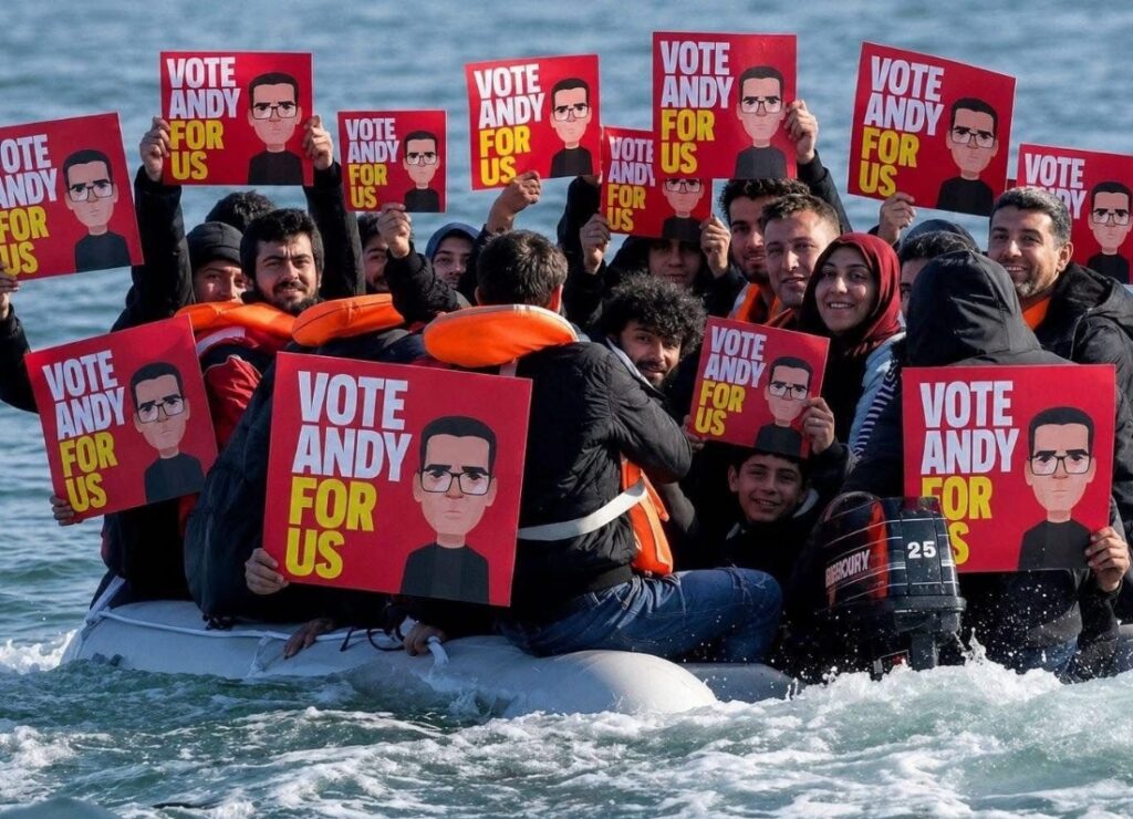 A crowded inflatable boat at sea carries people holding red signs featuring a cartoon image of Andy Burnham and the slogan "Vote Andy For Us".