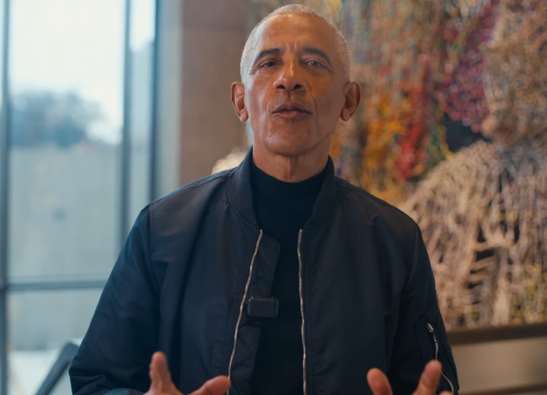 Barack Obama speaks directly to camera in a video message while standing indoors in front of a colourful artwork.