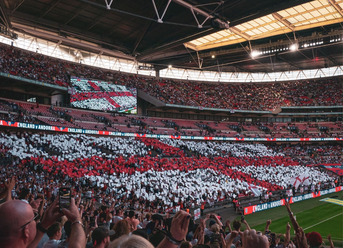 England supporters create a giant St George’s Cross display inside Wembley Stadium during an international match against Andorra, with thousands of fans holding red and white cards beneath the stadium roof.
