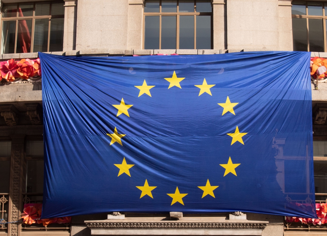 A large European Union flag hangs across the facade of a building decorated with festive lights and ornaments.