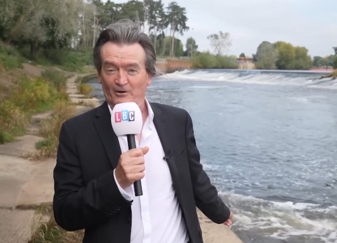 Environmental campaigner Feargal Sharkey speaks into an LBC microphone beside a river while discussing water industry issues.