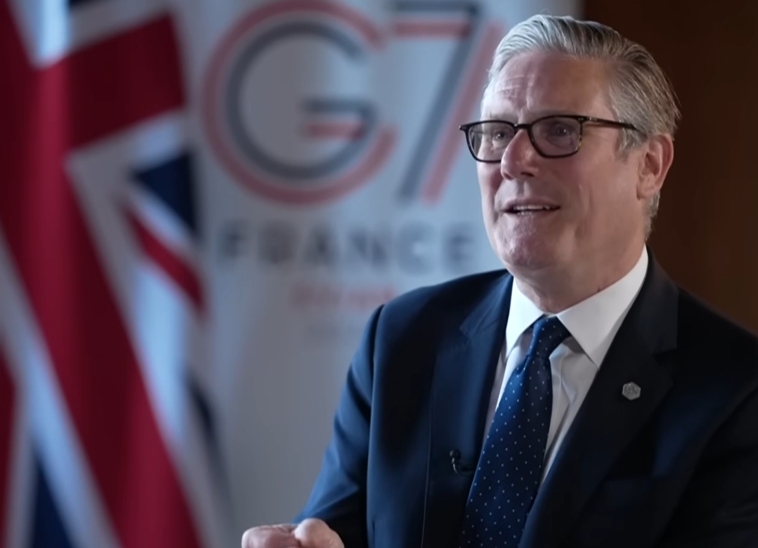 Prime Minister Keir Starmer speaks during an interview at the G7 summit with a UK flag visible in the background.