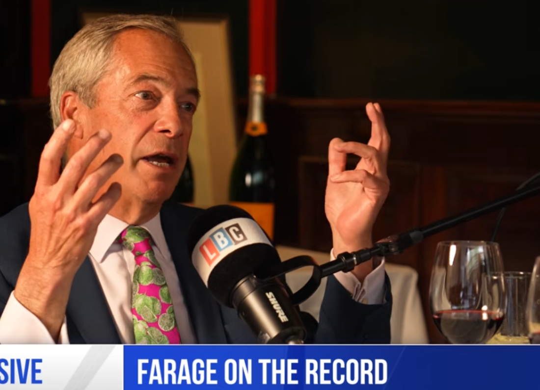 Nigel Farage speaks animatedly into an LBC microphone during a recorded interview, gesturing with both hands while discussing politics and current affairs.