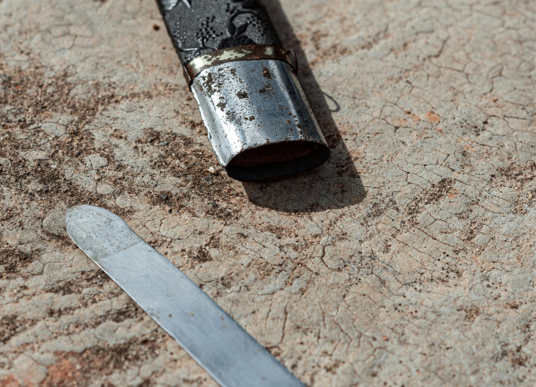 Close-up image of a kirpan lying on a rough concrete surface. The blade is partially exposed beside its decorative sheath.