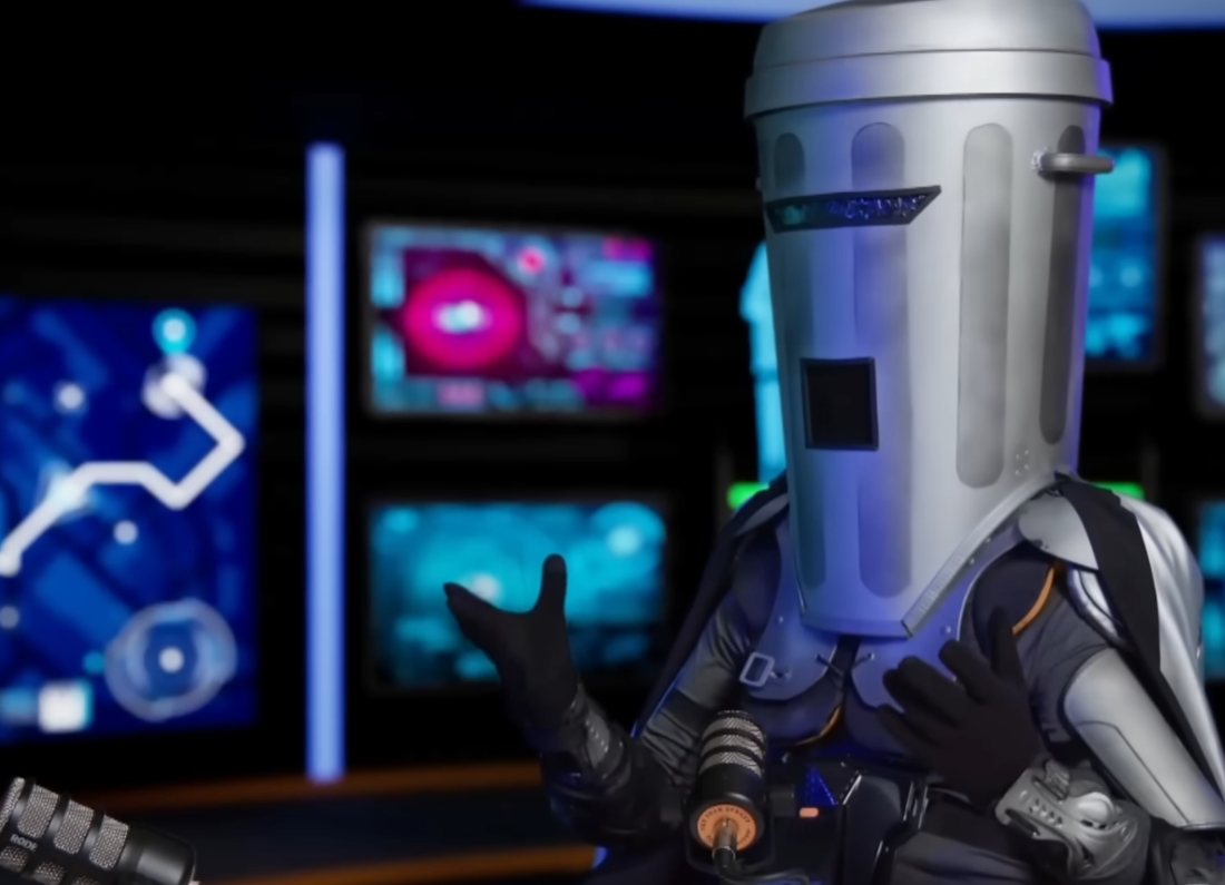 Count Binface wearing his silver bin-shaped costume while speaking into microphones during a television interview.