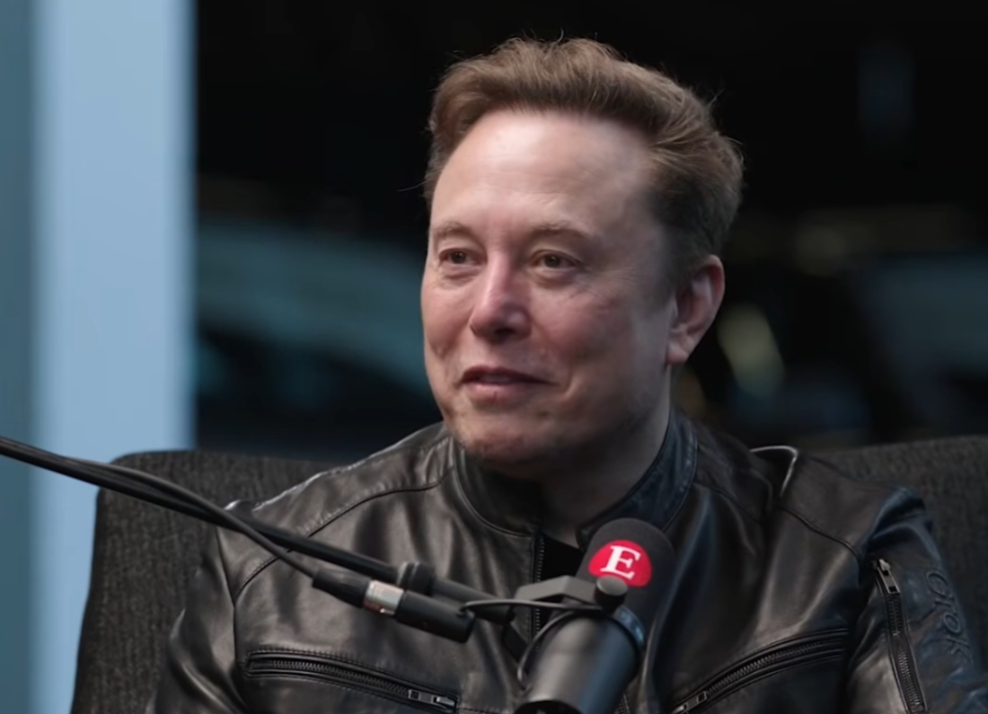 Elon Musk speaking into a microphone during an interview with The Economist.