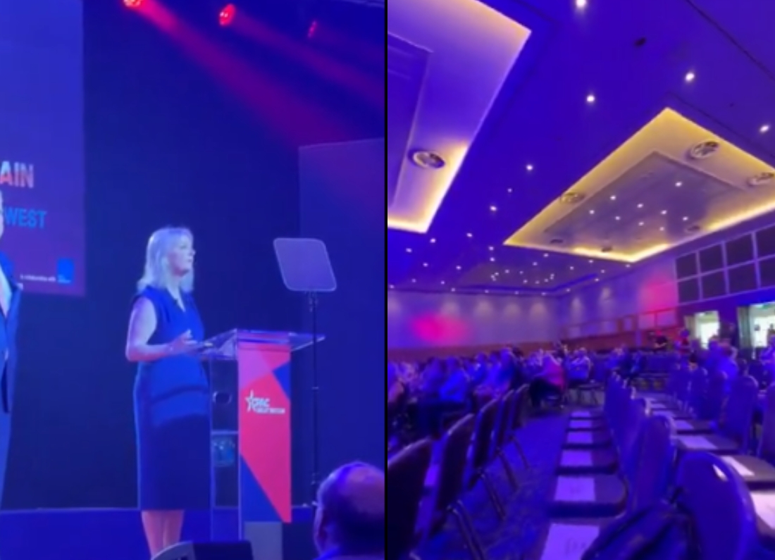 Liz Truss speaks on stage at CPAC GB in London beside a view of rows of empty seats in the conference hall.