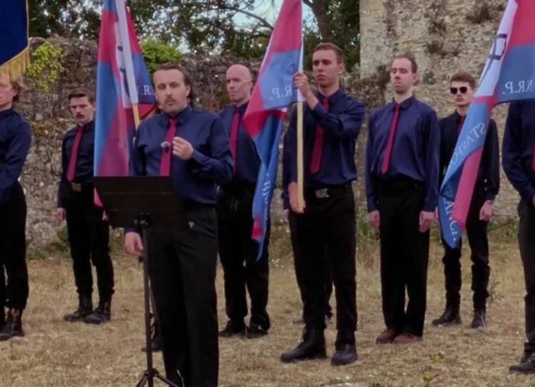 National Rebirth Party members in navy shirts and red ties marching with flags and a drum at an Oxfordshire event