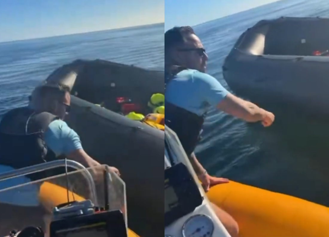Danny Tommo leaning from a boat towards an inflatable dinghy during a rescue operation in the English Channel
