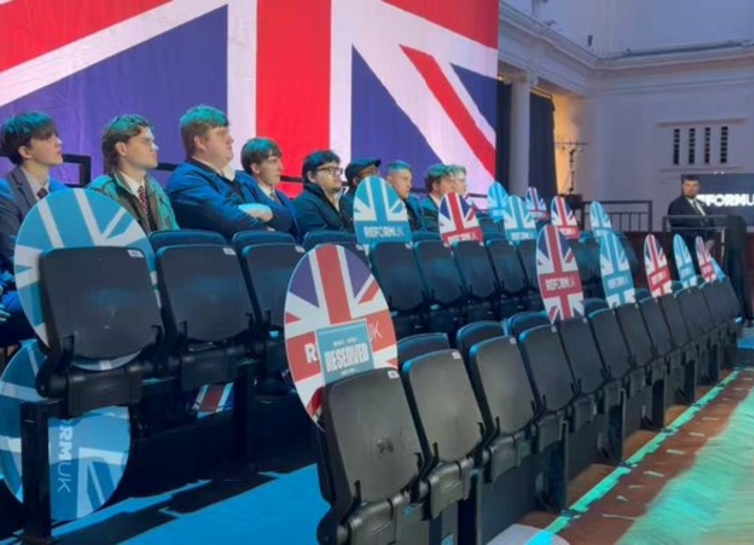 Rows of empty seats at Reform UK's Westminster economic event on 26 October 2026, with a large Union Jack backdrop and Reform-branded signs.